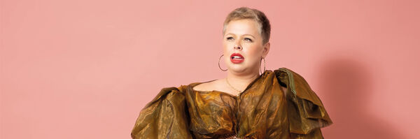 Laura Smyth wearing an olive dress with puffy sleeves in front of a pink background