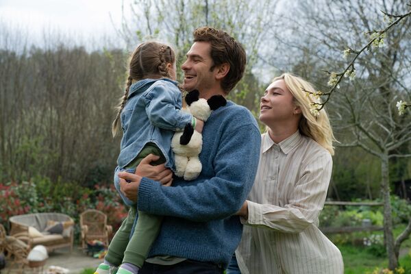 A young father holding his daughter as the mother stands behind looking on lovingly. 