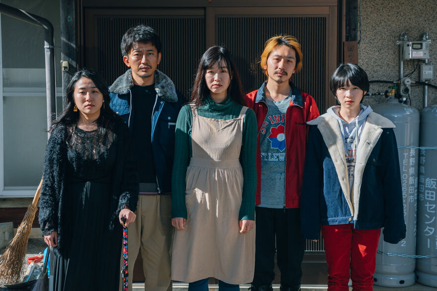 A family stand side by side in front of a house. 