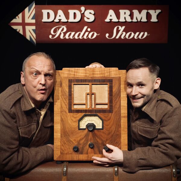 Two men in army uniform with an old fashioned radio and a sign behind with a Union Jack Arrow saying 'Dad's Army Radio Show'