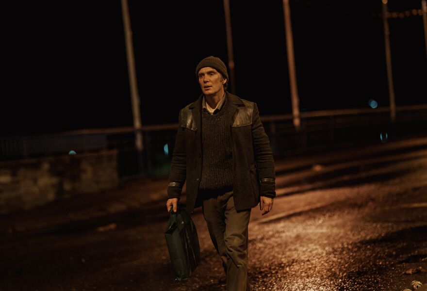 A man walks alone down a dark road carrying a bag. 