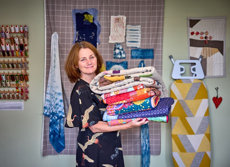 Julia O'Connell standing in a sewing room holding a pile of folded quilts.