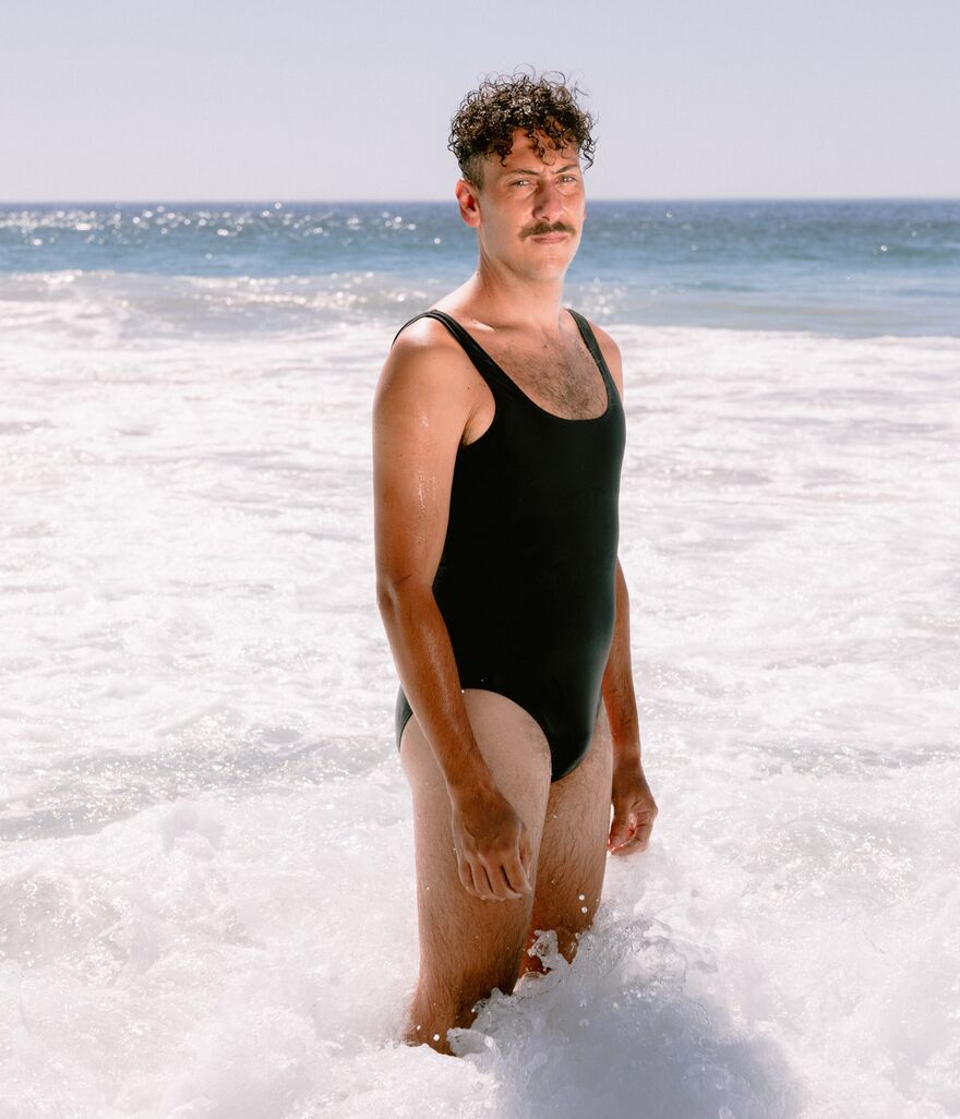 Man stood in a one-piece swimsuit, knee deep in the sea  