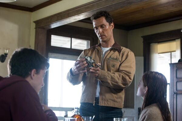 A man stares at a miniature model of a spacecraft as two children look on. 