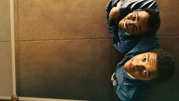 Two young men in prison uniforms look up smiling. 