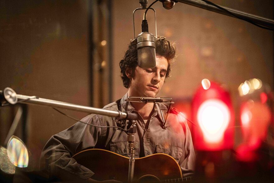 Timothée Chalamet as Bob Dylan, holding a guitar behind a mic. 