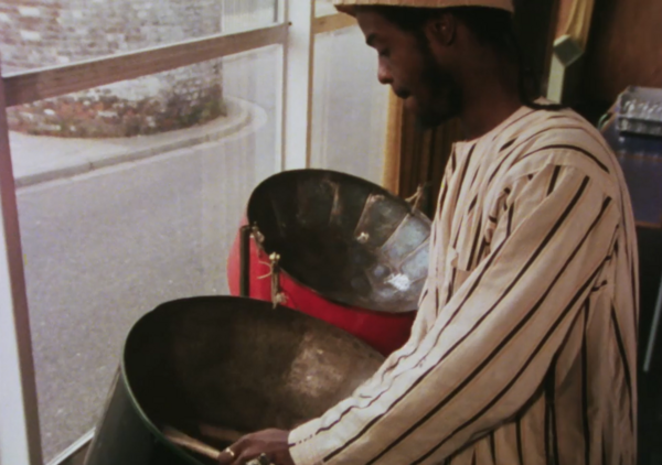 A man plays steel drums next to a window. 