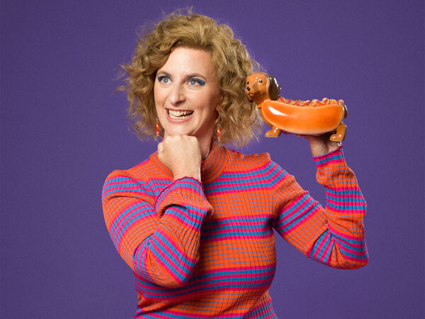 Woman smiling in red and blue striped dress in front of purple background.